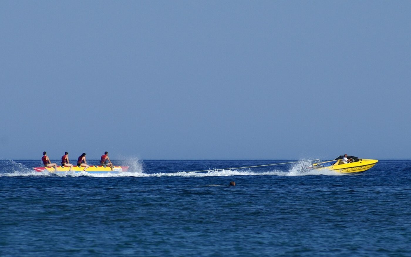 Banana boat with riders being towed by a speedboat across the open sea