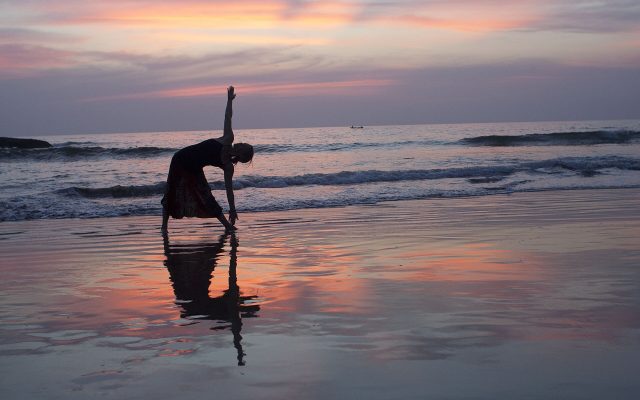 Silhouette of a person in a yoga pose at the water's edge on a beach at sunset