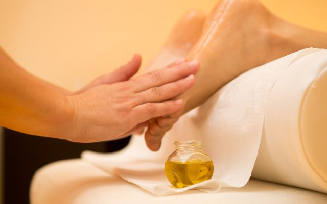 Hands applying pressure to the sole of a foot during a reflexology treatment with massage oil