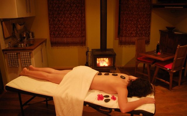 Guest relaxing face down on a massage table during a hot stone massage with flowers on the towel