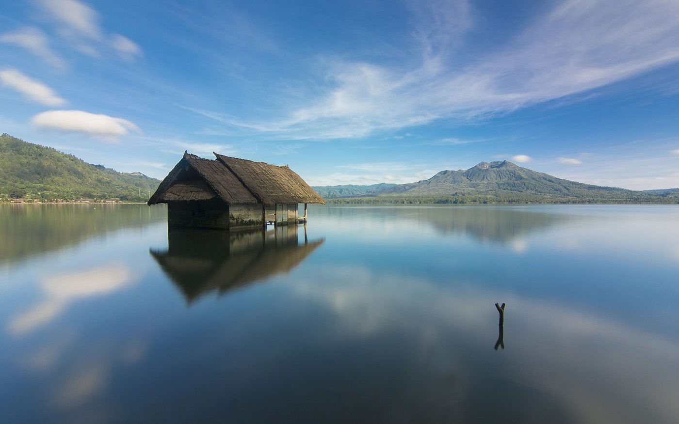 Wooden hut standing in calm Lake Batur with mountains reflected in the water, Kintamani