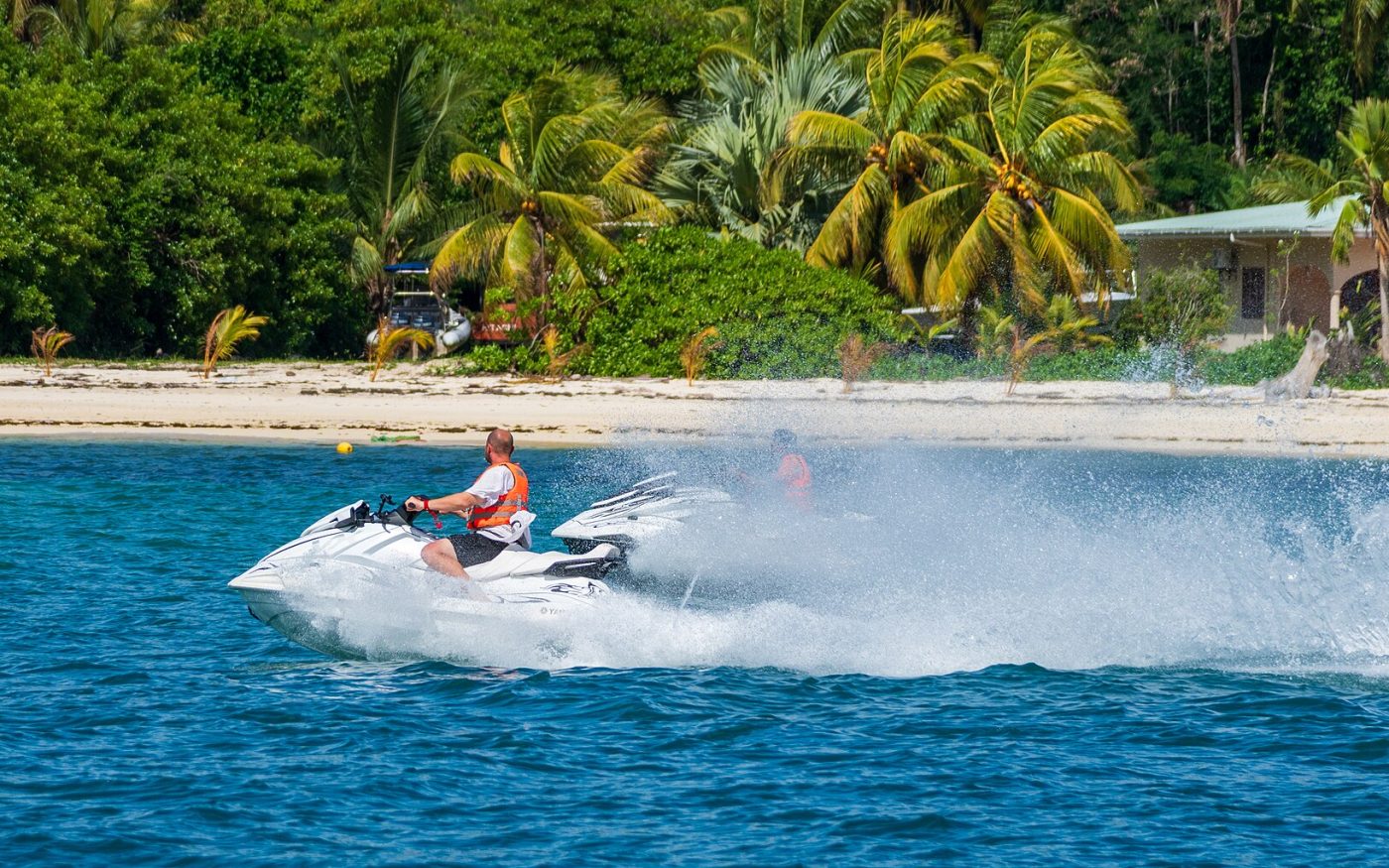 Jet ski speeding across turquoise water past a palm-lined tropical beach