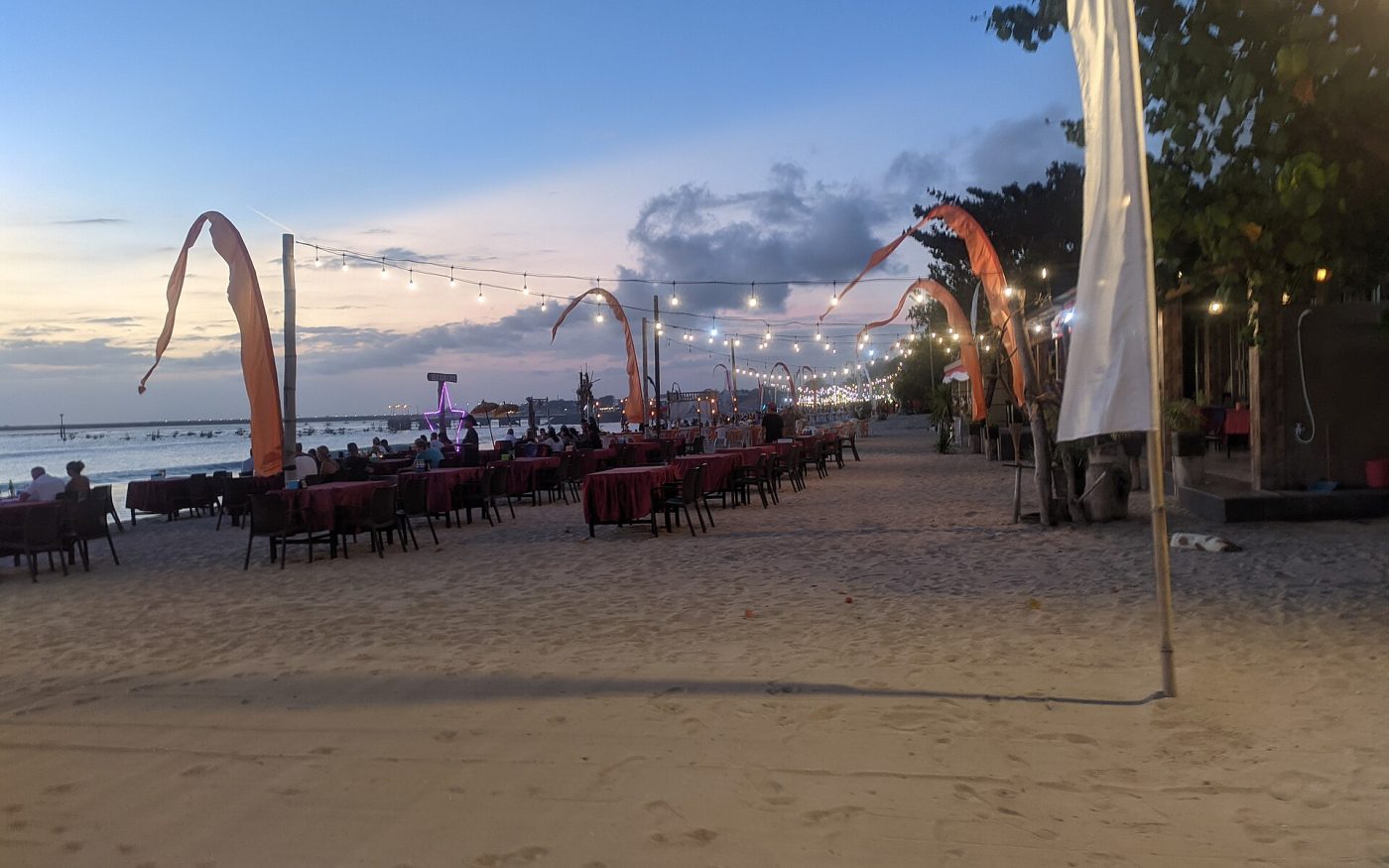 Dinner tables and lanterns lined up on the sand at a Jimbaran beachfront restaurant at dusk