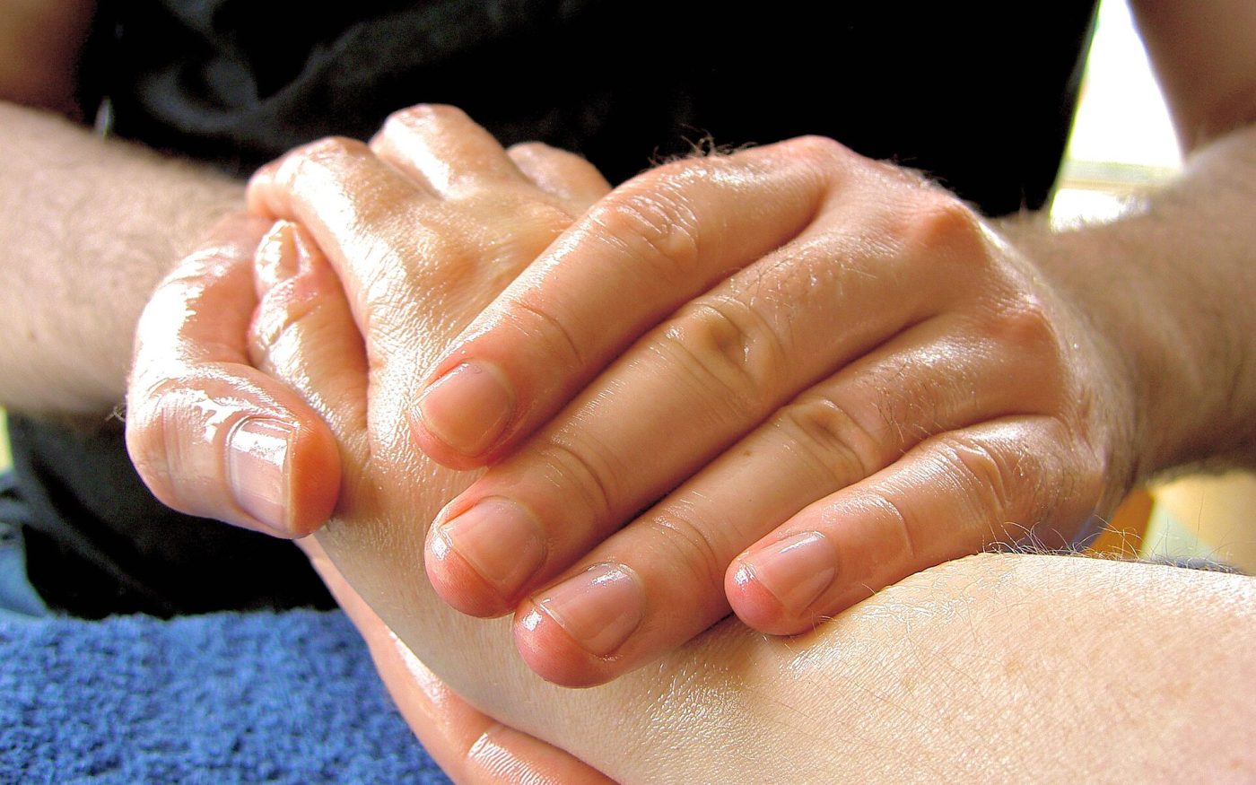 Close-up of a massage therapist's hands massaging a hand with oil