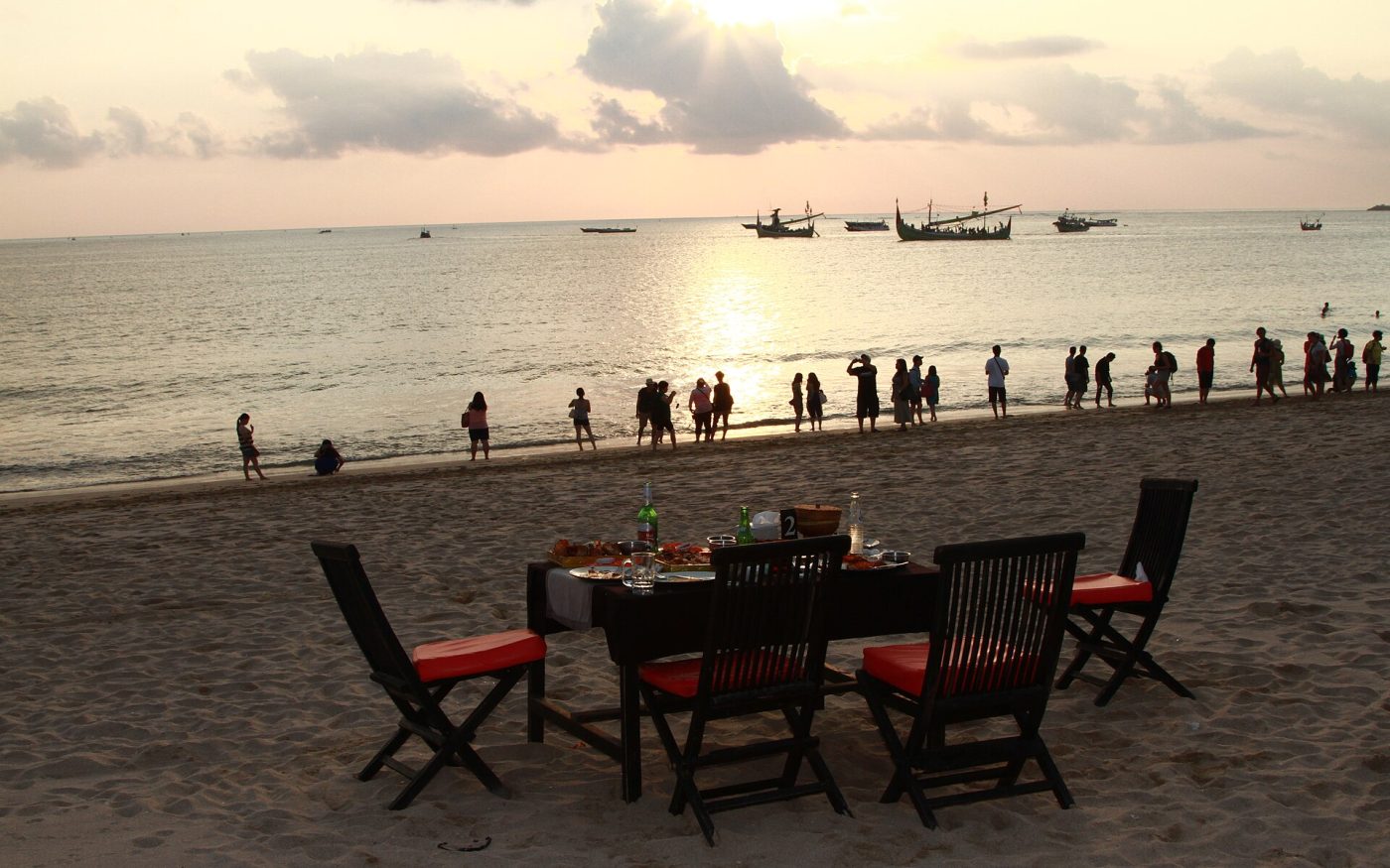 Table for dinner set on the sand at Jimbaran Beach with fishing boats and the sunset over the bay
