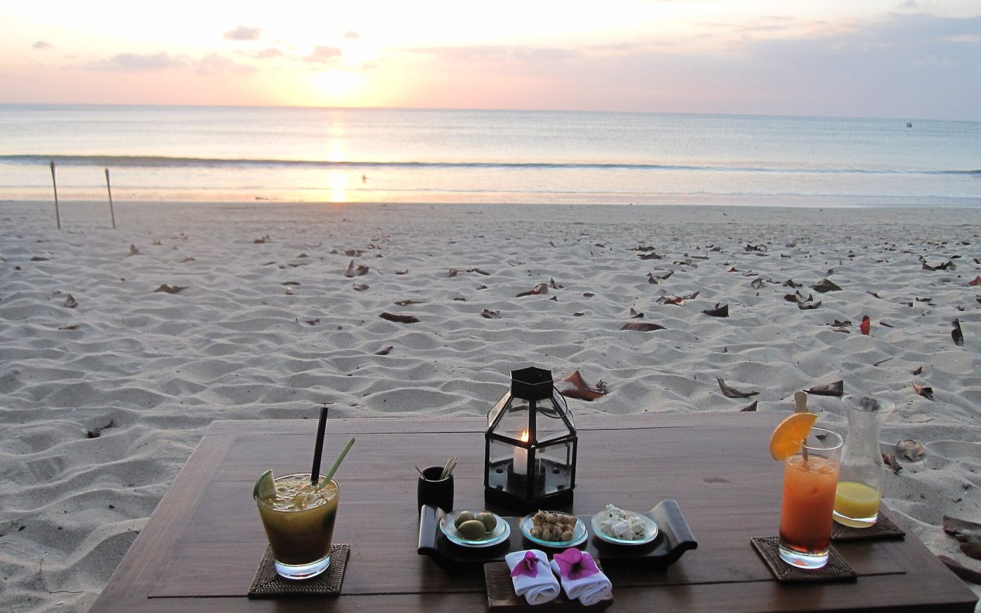Table with cocktails and a lantern on the sand at Jimbaran Beach at sunset