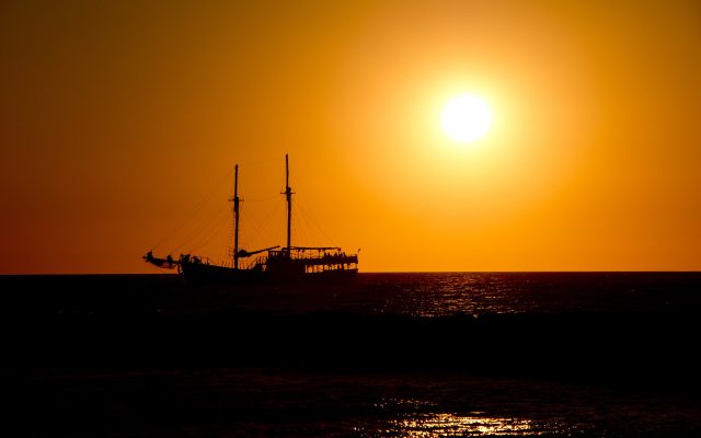 Silhouette of a tall sailing ship on a golden sea at sunset