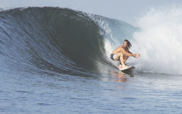 Surfer crouching on a board inside a curling blue wave in Indonesia