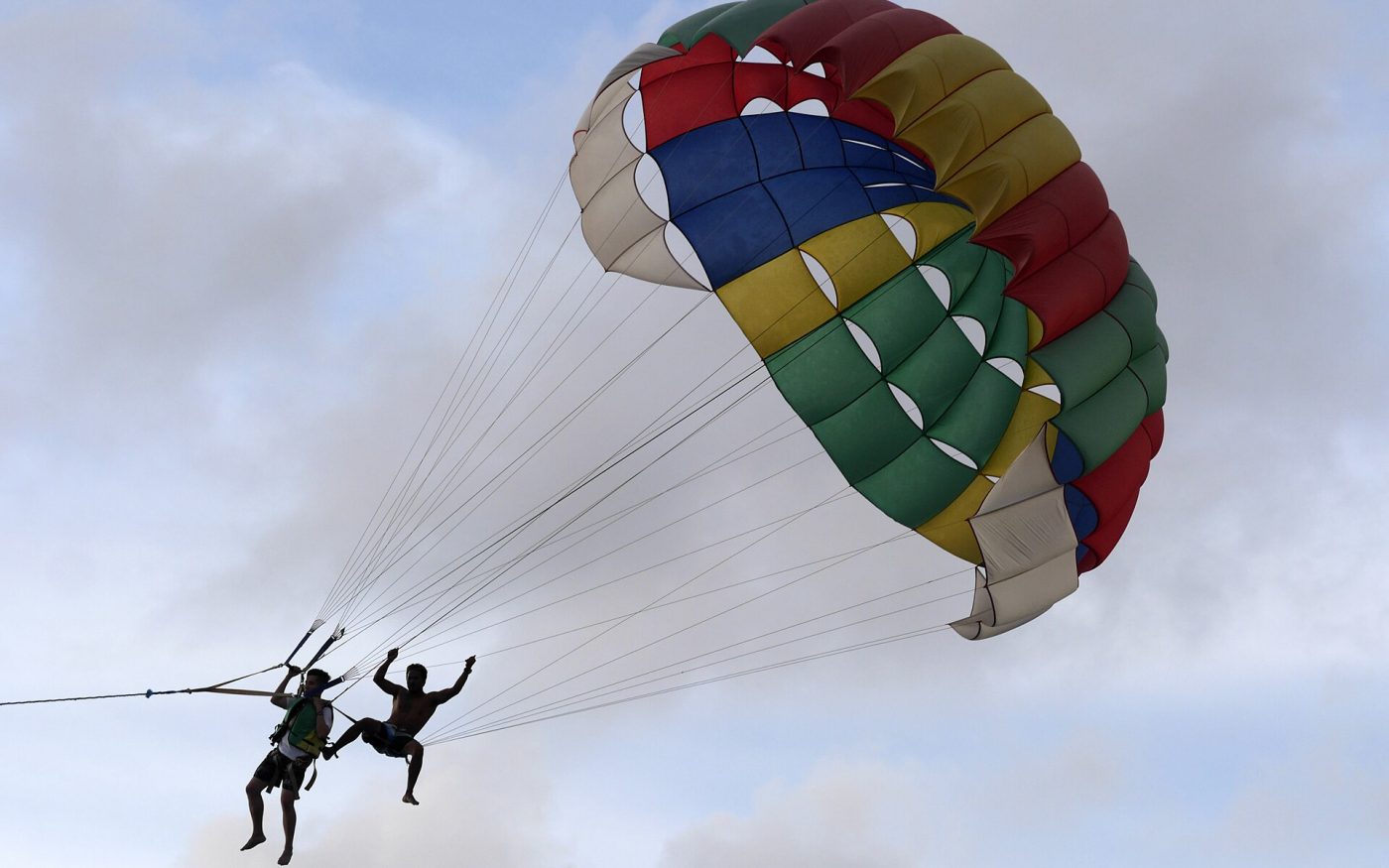 Two people parasailing under a colourful parachute against a blue sky
