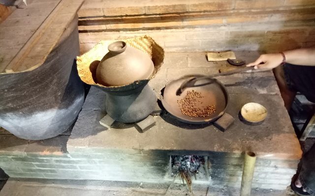 Coffee beans being roasted in a clay pan over a wood fire at a Balinese coffee plantation