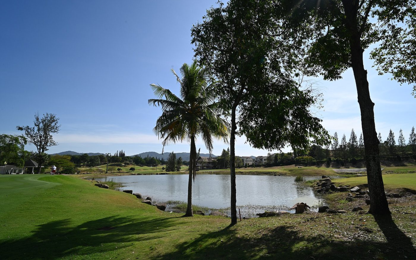 Sunlit tropical golf course with a calm pond framed by palm trees under a blue sky
