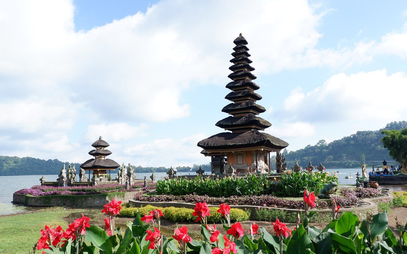 Multi-tiered meru shrine of Ulun Danu Beratan temple on Lake Beratan with red flowers in the foreground