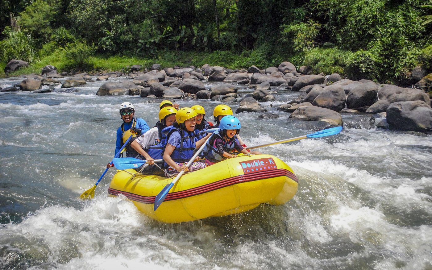 Rafting team with helmets and paddles riding a grade 2 rapid on a tropical river in Indonesia